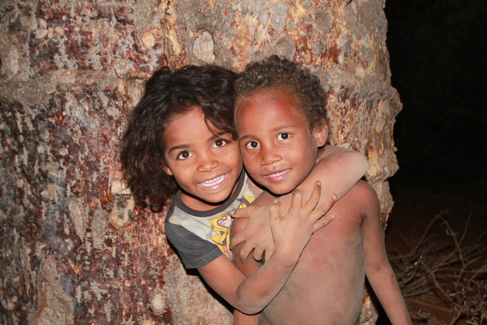 Deux enfants souriants enlacés devant un mur de pierre, à Madagascar