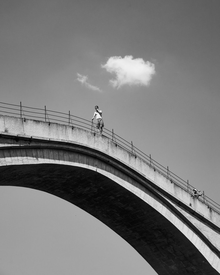 Cycliste franchissant un pont en arc, en noir et blanc, un seul nuage dans le ciel